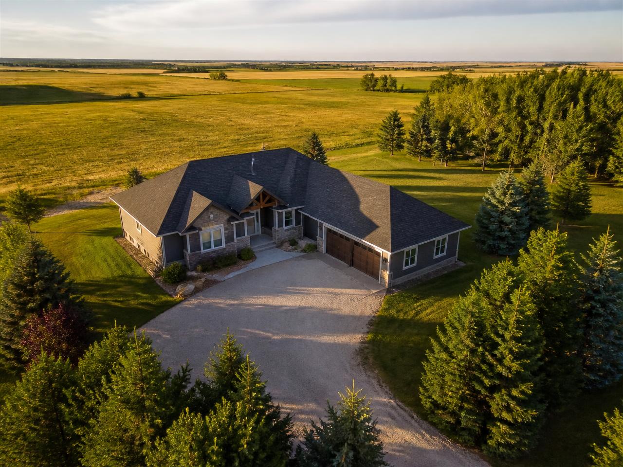 Aerial view of a prairie acreage home, driveway, and yard with open fields beyond